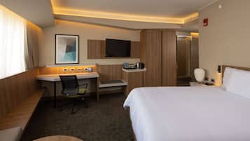 A hotel room with a bed, desk, chair, TV, and a bathroom door.