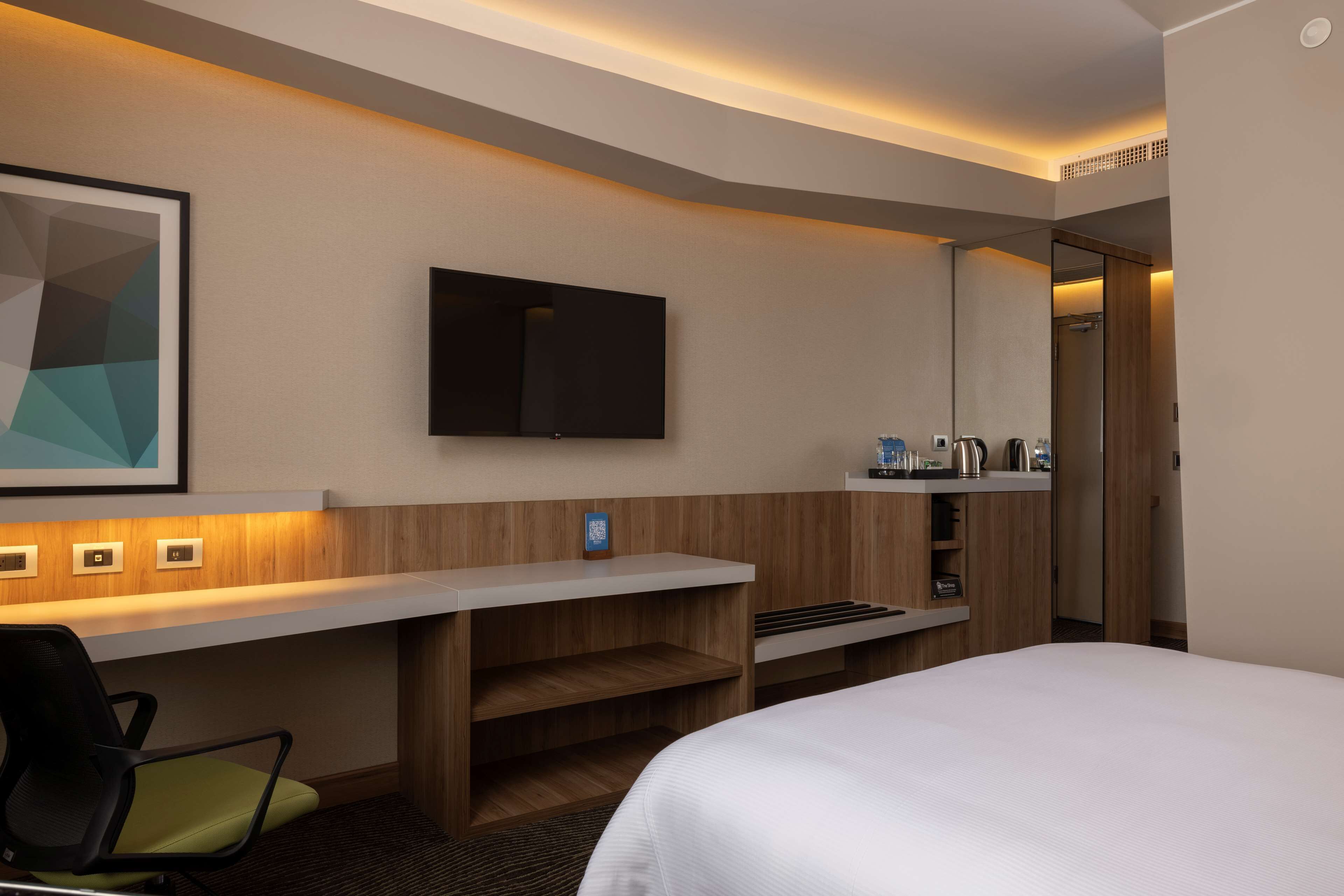 A hotel room with a bed, a desk with a chair, a television, and a minibar.