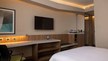 A hotel room with a bed, a desk with a chair, a television, and a minibar.