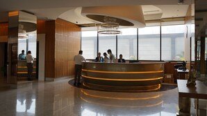A modern reception area with a curved reception desk, large windows, and a chandelier. - Hilton Garden Inn Pune Hinjawadi (Paud)