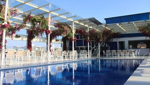 A pool area with clear glass roofing, white lounge chairs, and a pool. - Hilton Garden Inn Pune Hinjawadi (Paud)
