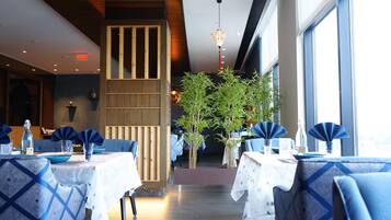 A restaurant with tables set for dining, wooden paneling, and potted plants.