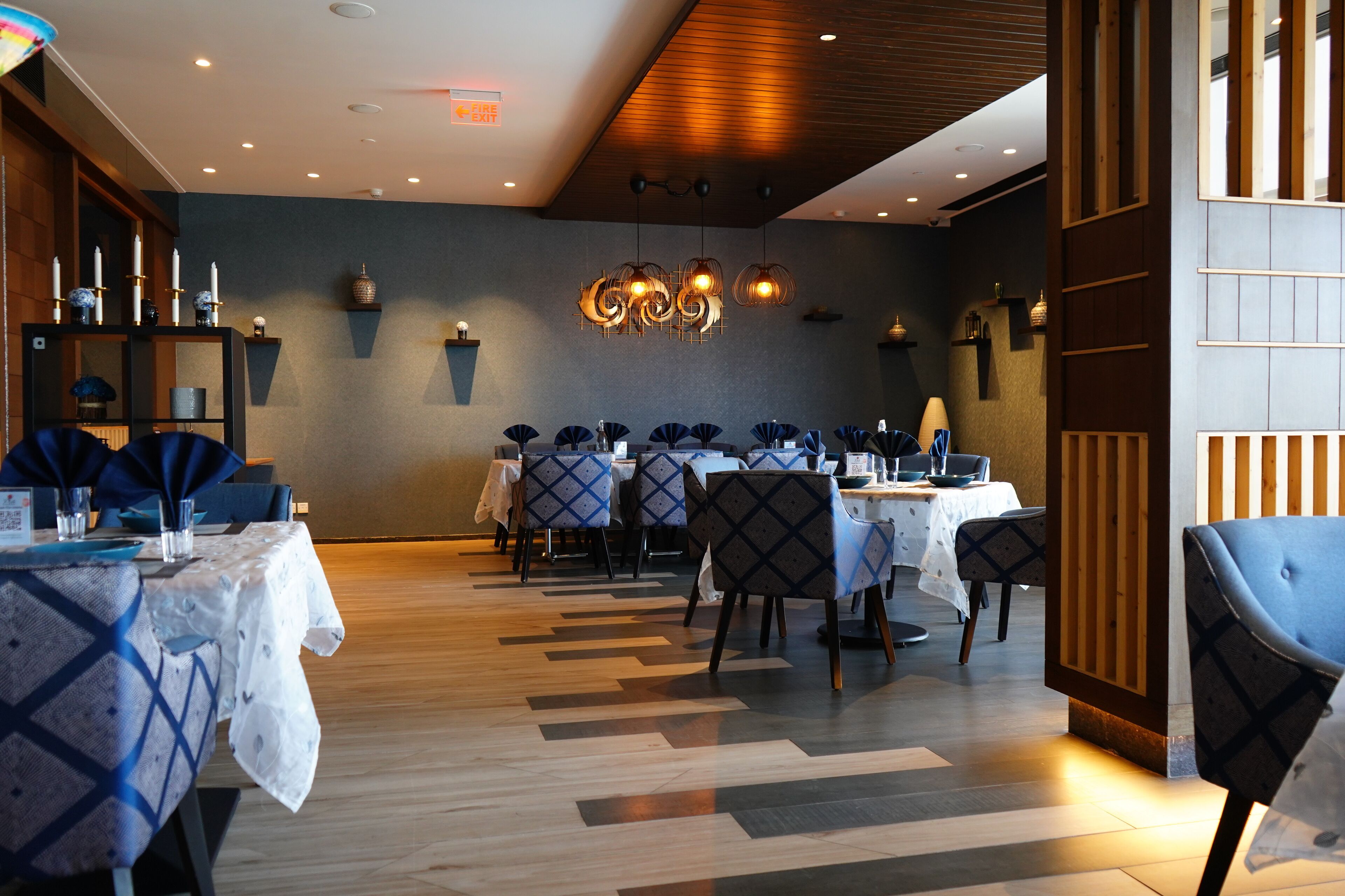A restaurant with tables set for dining, a patterned floor, and pendant lighting.