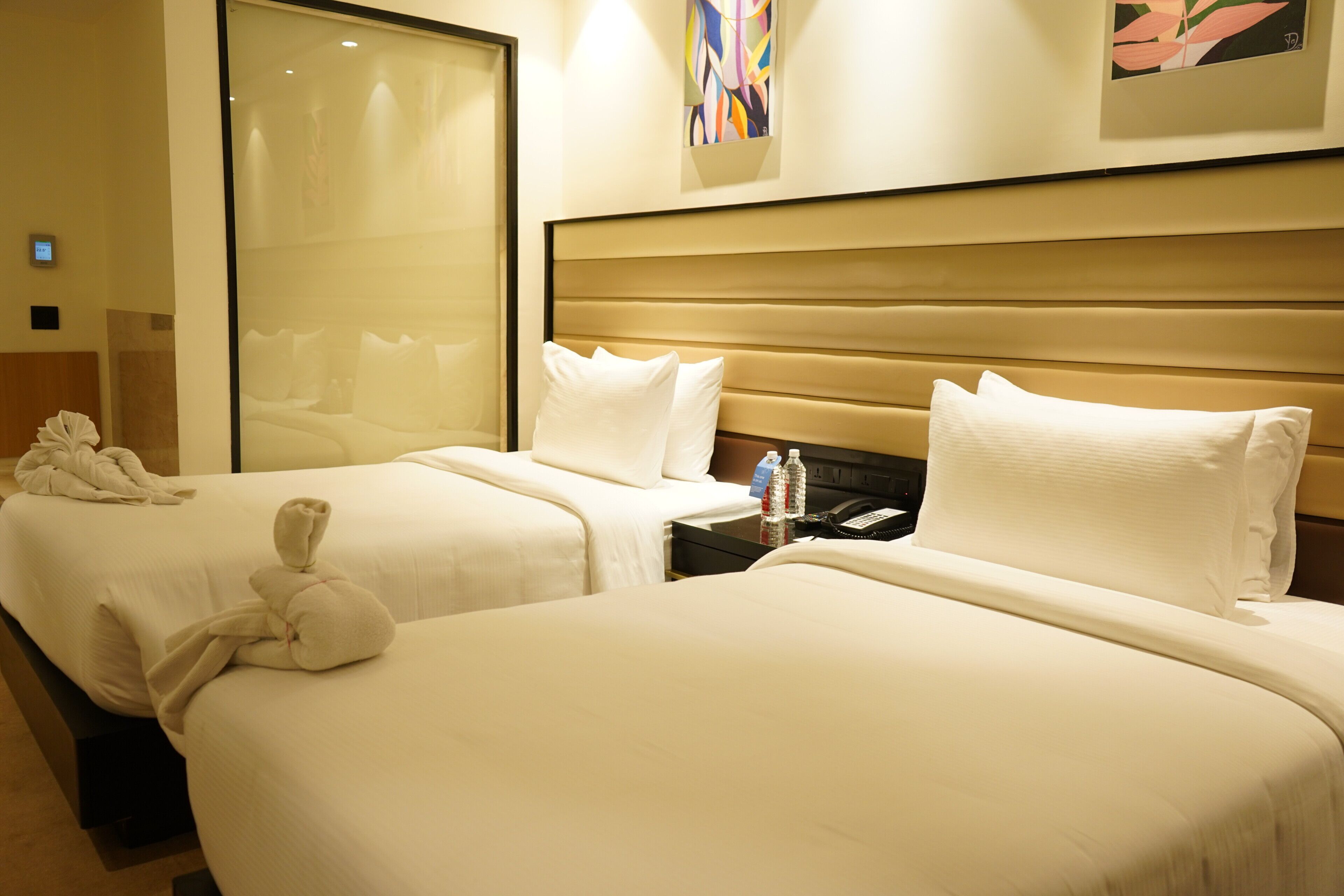 Habitación de hotel con dos camas, una mesita de noche con teléfono y botellas de agua, y un ventanal grande.