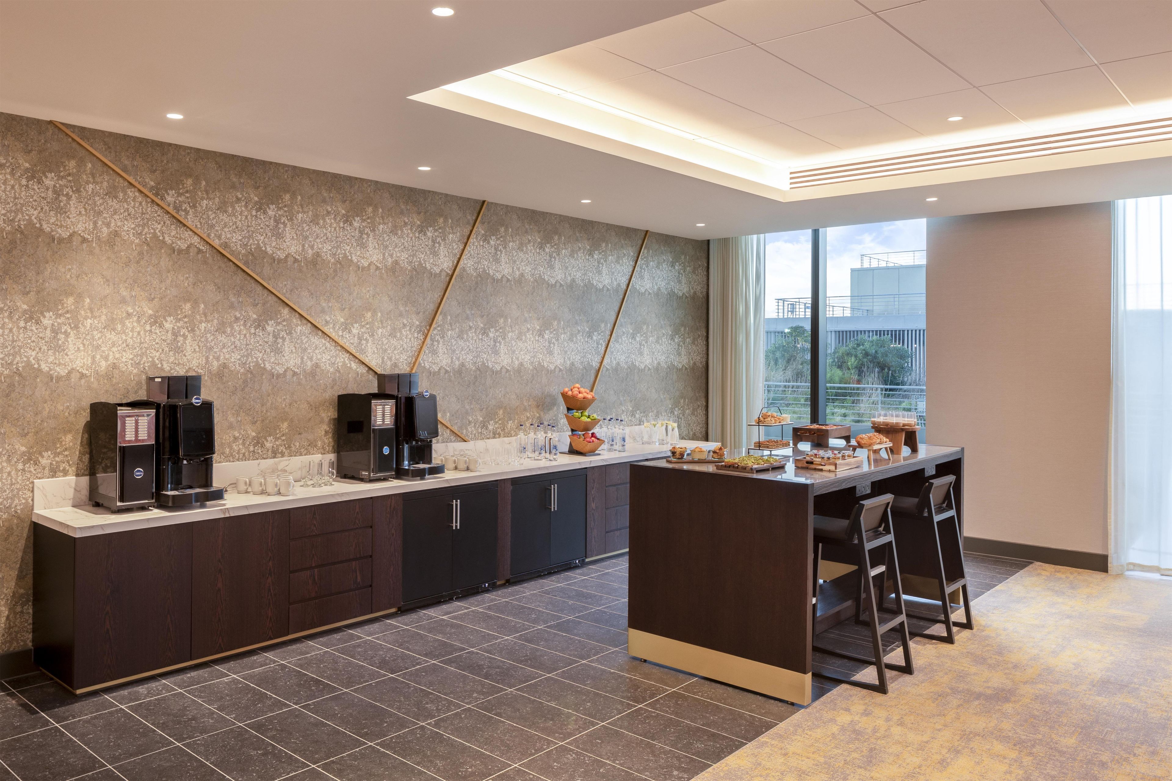 A modern kitchen area with a coffee station, bar stools, and a view of the outside.