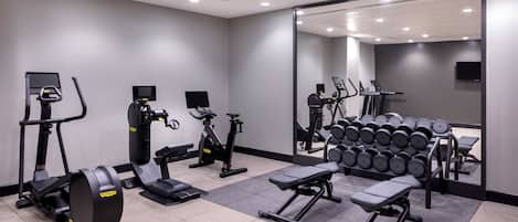 A modern gym with cardio machines, weight benches, and dumbbells.
