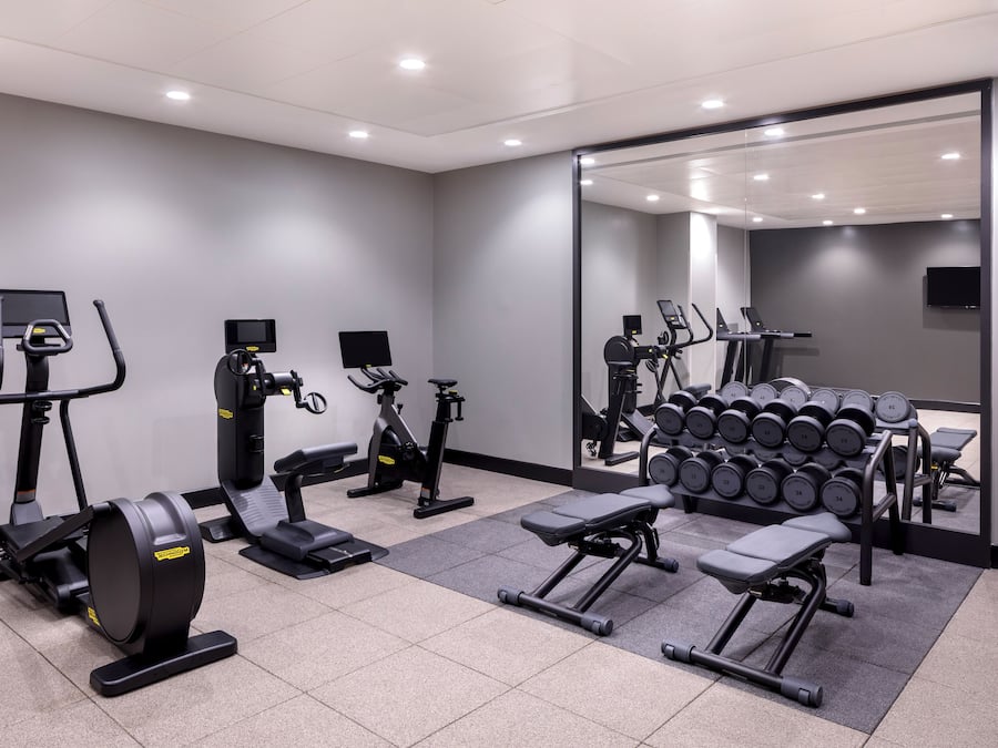 A modern gym with cardio machines, weight benches, and dumbbells.