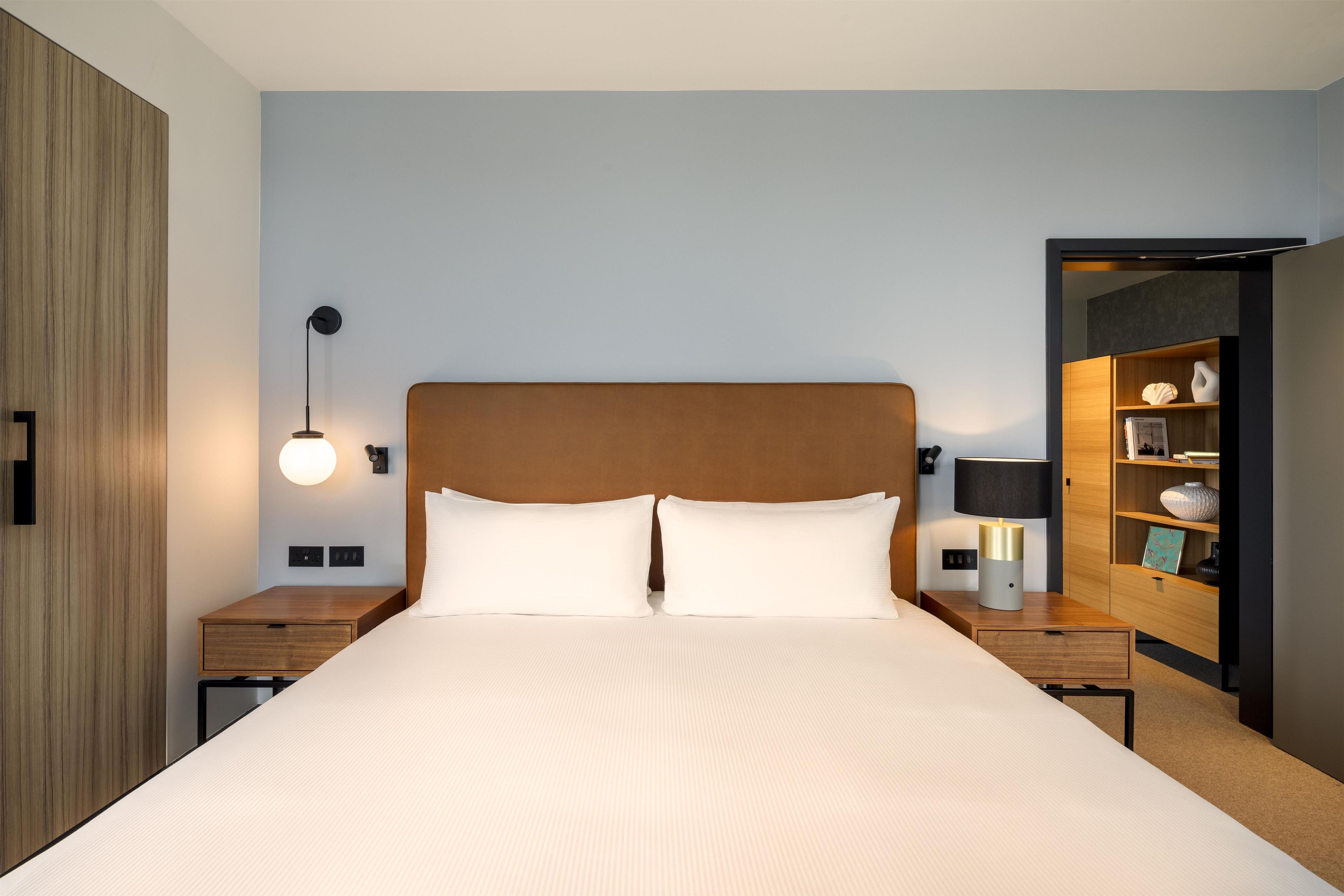 Een hotelkamer met een groot bed, nachtkastjes, een wandlamp en een houten garderobe.