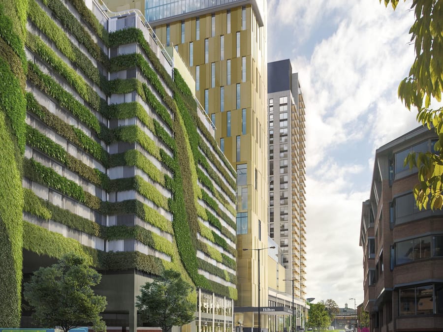 Un edificio moderno con fachada verde, entrada de vidrio y un letrero visible de 'Hilton'.