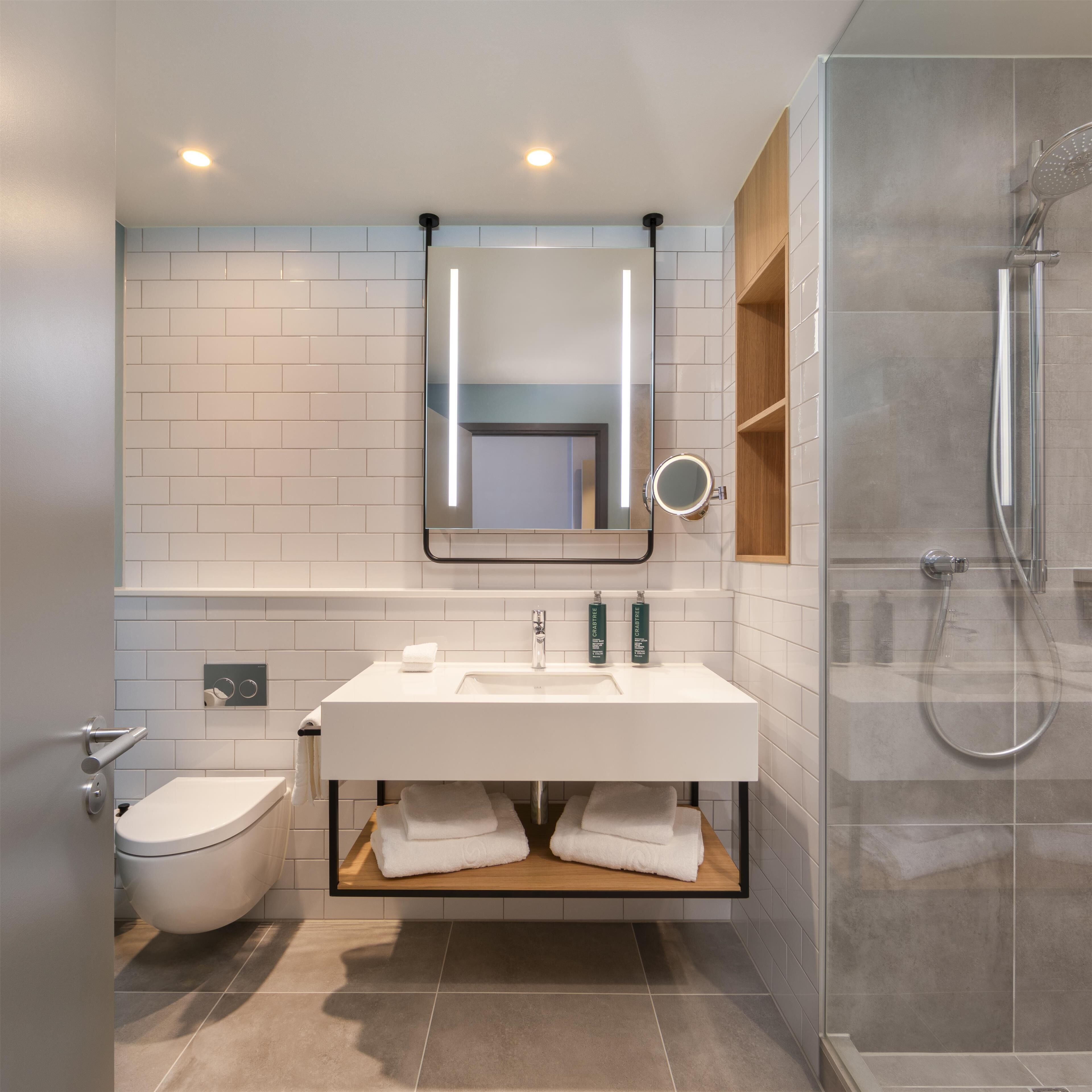 A modern bathroom with a white sink, mirror, and toilet.