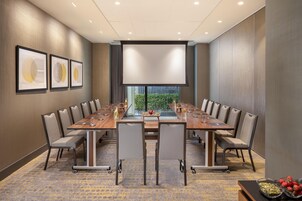 Un salón de conferencias con una larga mesa, sillas y una pantalla de proyector.