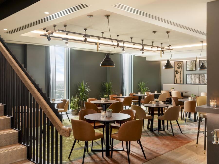 Een modern interieur met een trap, meerdere eettafels en stoelen.