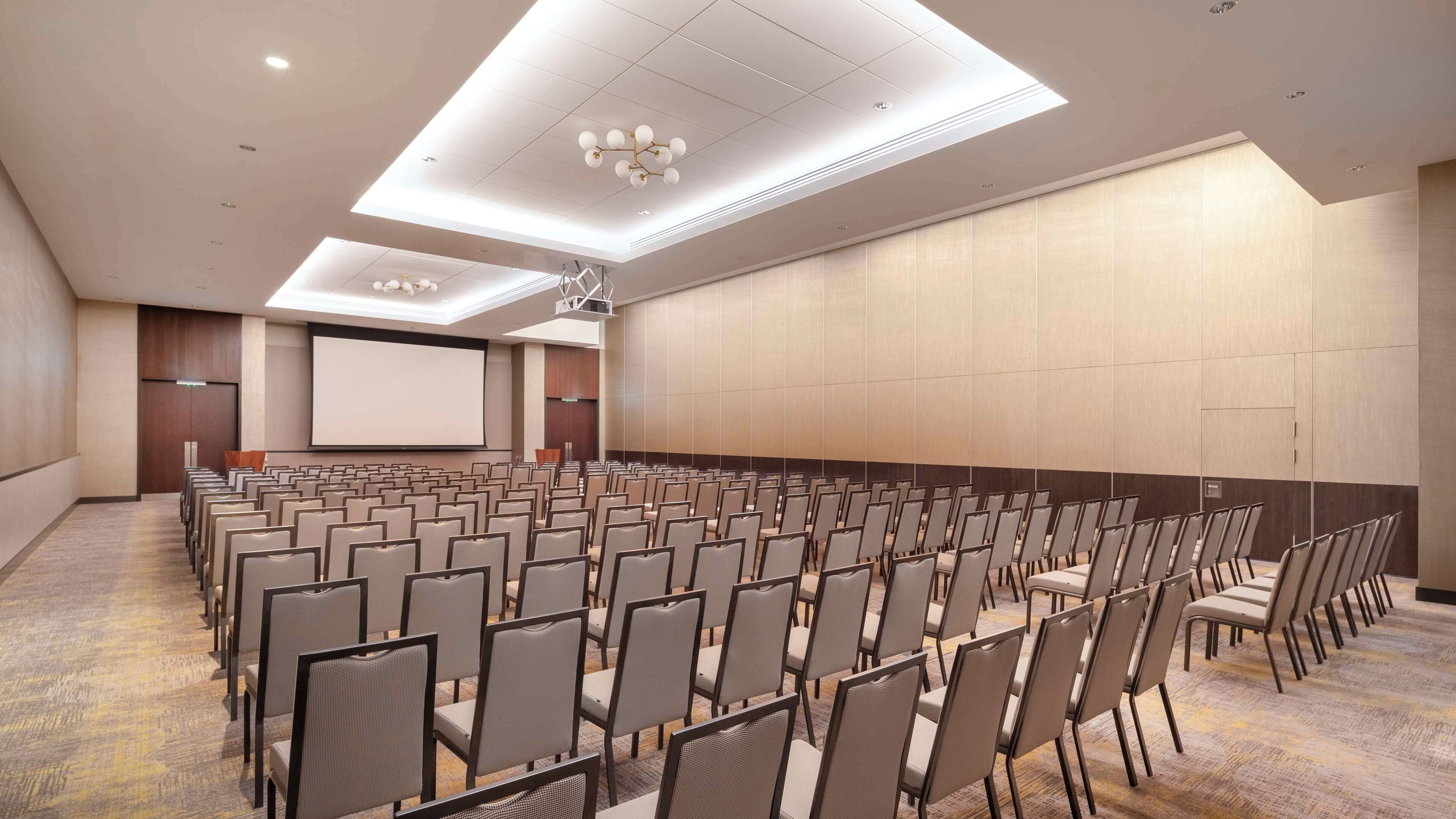 A conference room with rows of chairs, a large screen, and a projector.