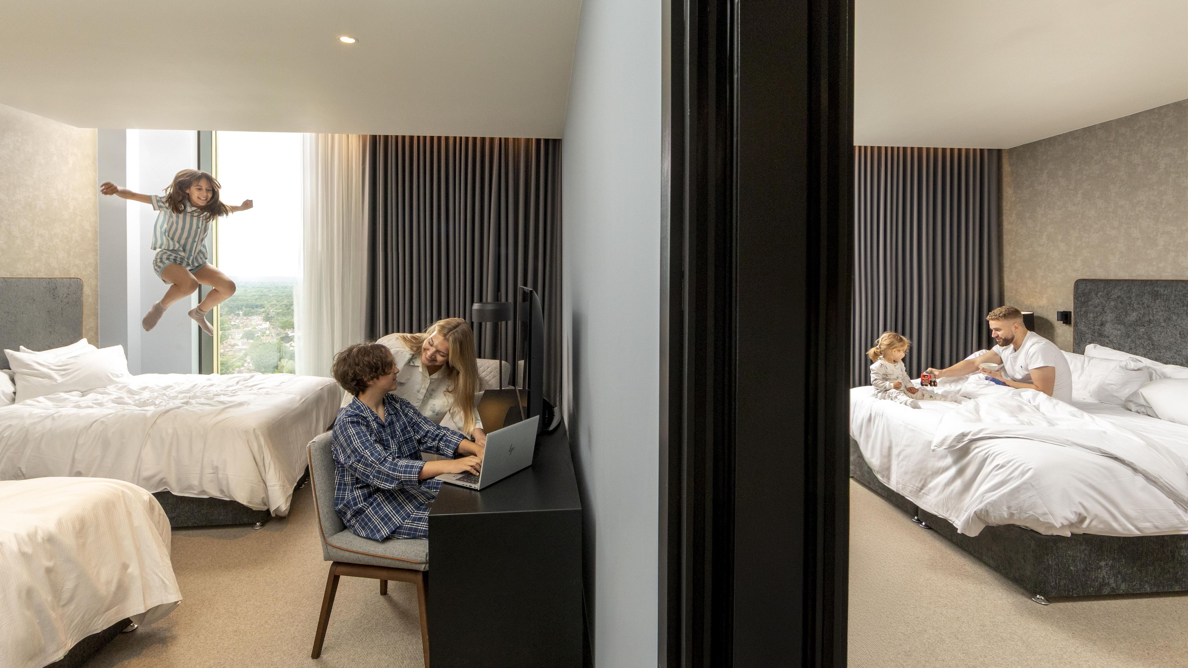 Habitación de hotel con dos camas, un escritorio con una computadora portátil, un televisor y una ventana con cortinas.