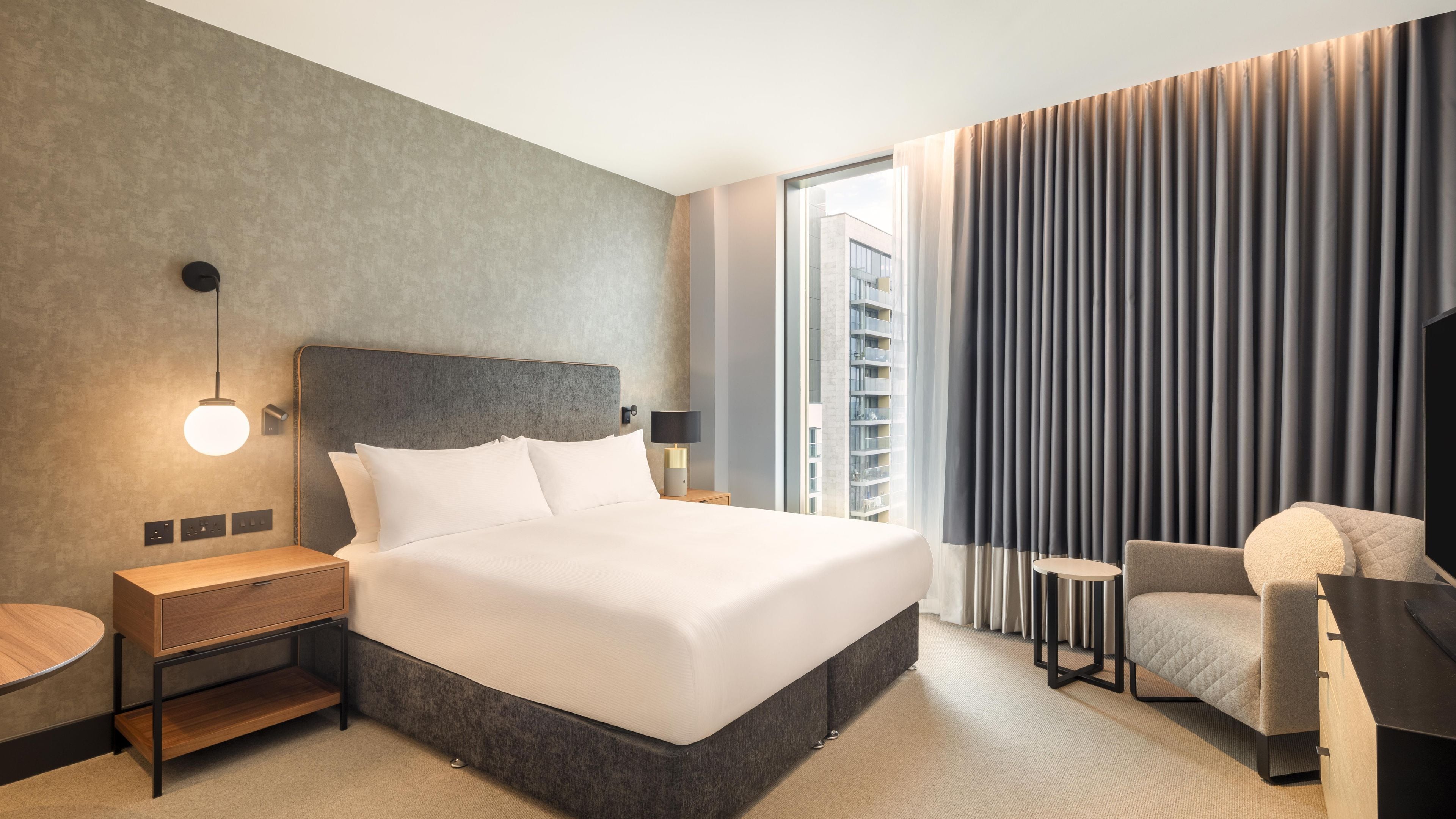 Una habitación de hotel moderna con una cama grande, mesitas de noche, un escritorio y una silla.