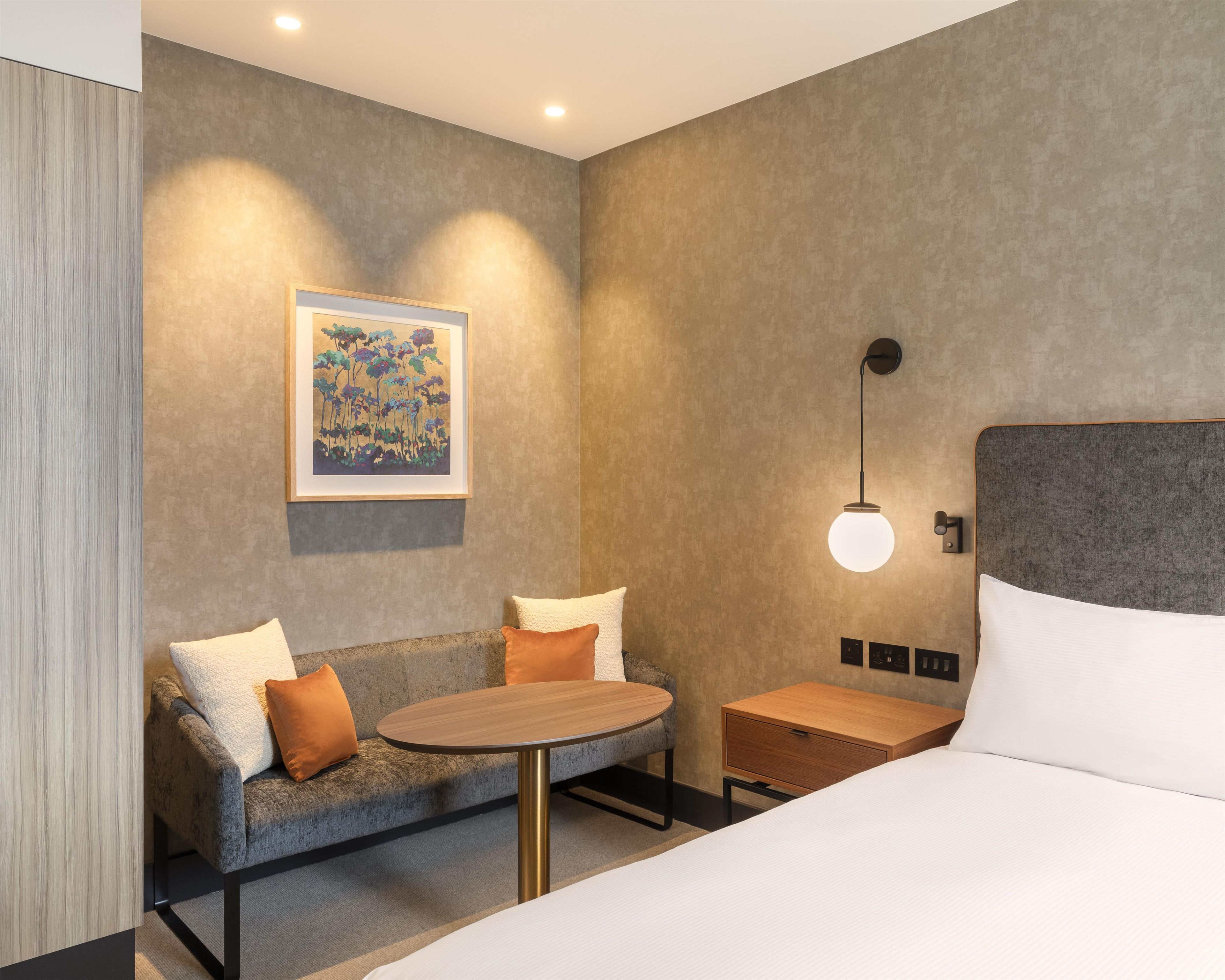 Una habitación de hotel moderna con un sofá, una mesa redonda, una cama y un cuadro en la pared.