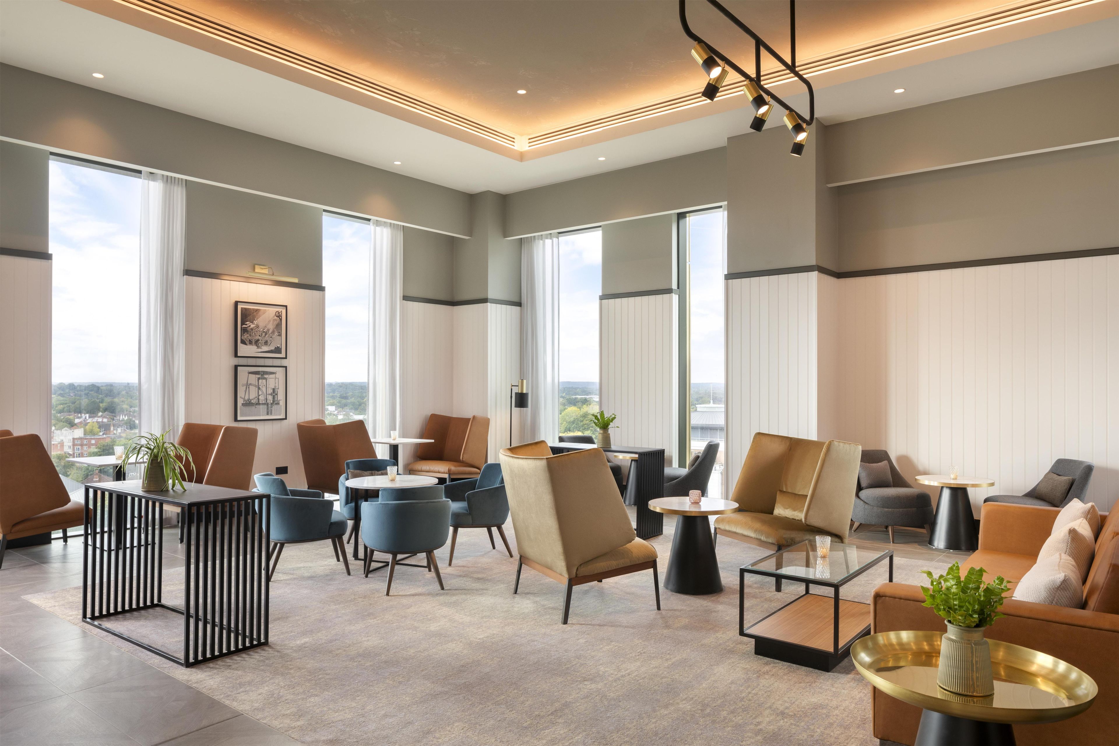 Ett rymligt loungeområde med flera olika sittplatser, stora fönster med fin utsikt och en modern takdesign.