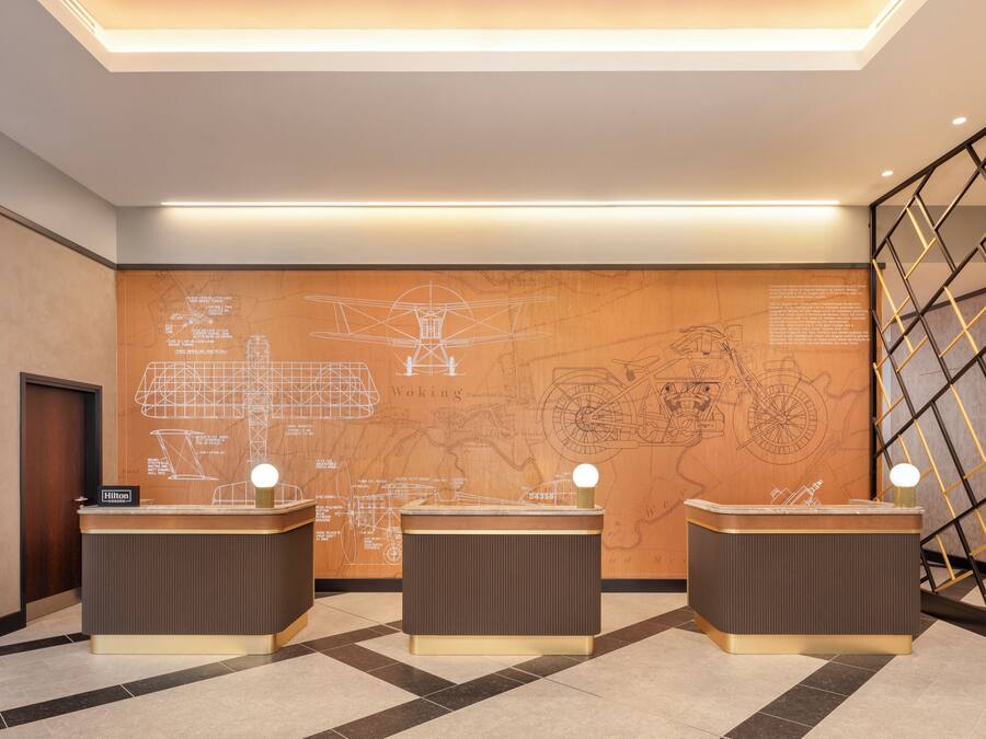 A reception area with three counters, a large wall with architectural drawings, and a modern staircase.