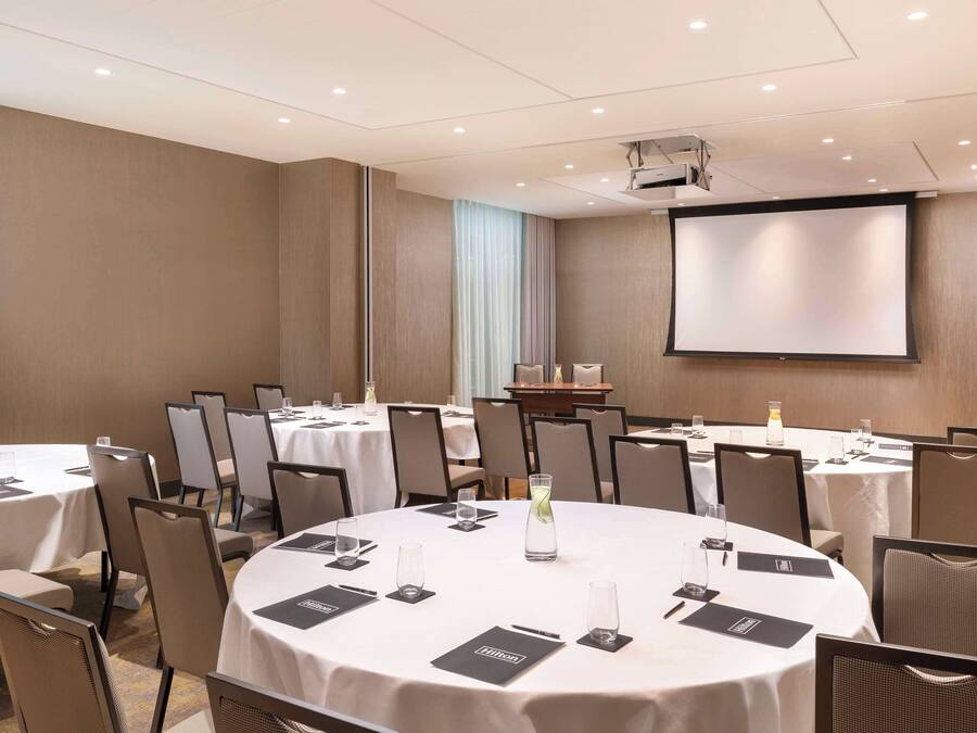 A conference room with round tables, chairs, a projector screen, and a large screen.