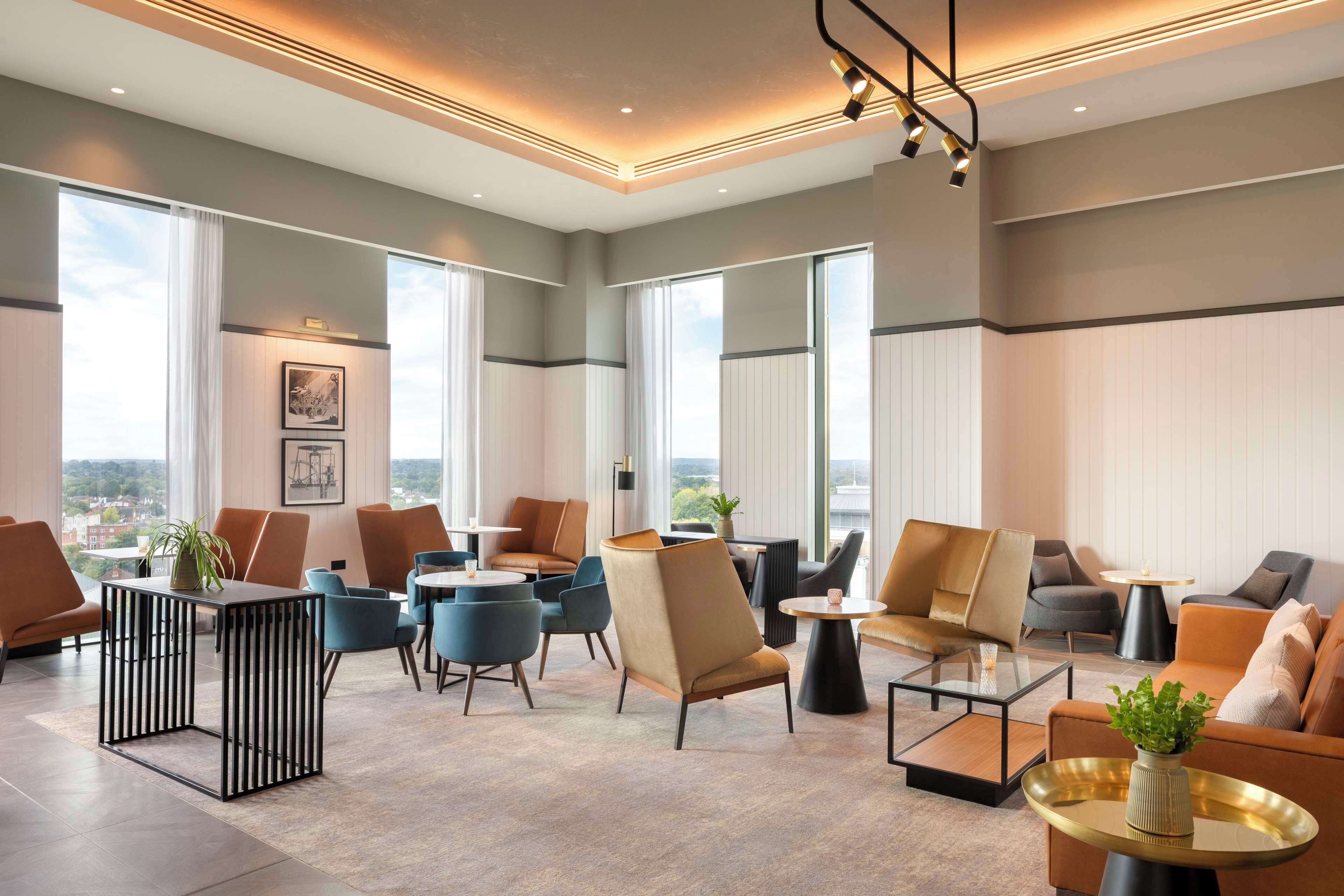 Un moderno vestíbulo de hotel con diversas opciones de asientos, ventanas amplias y vistas a la ciudad.