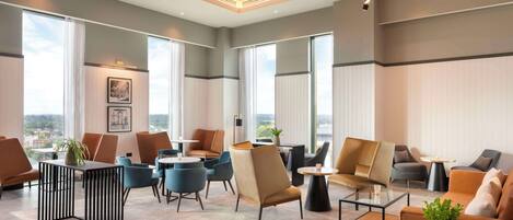 Un moderno vestíbulo de hotel con diversas opciones de asientos, ventanas amplias y vistas a la ciudad.