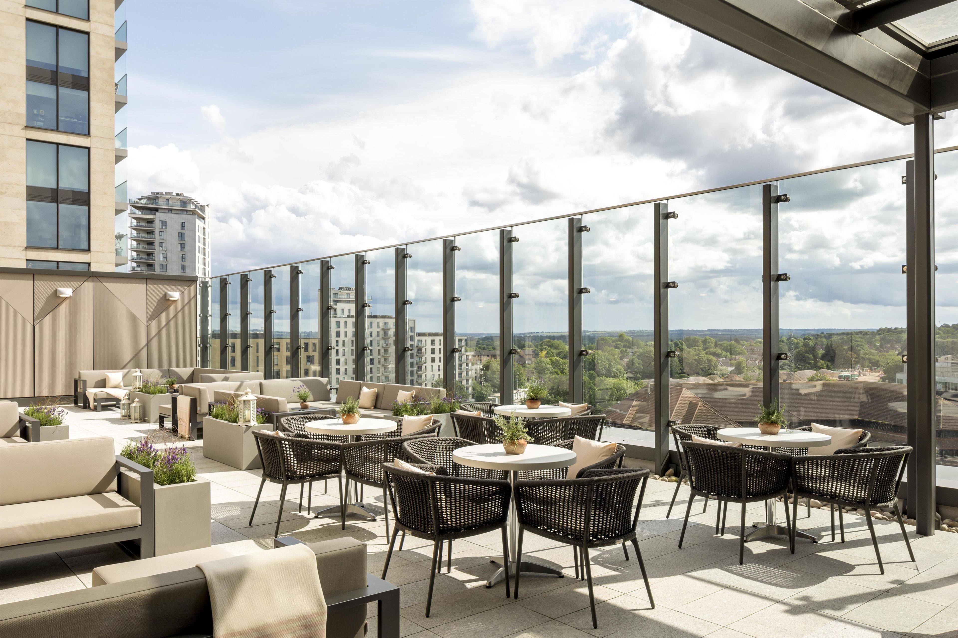 Een terras op het dak met buitenmeubilair, grote ramen en uitzicht over de stad.