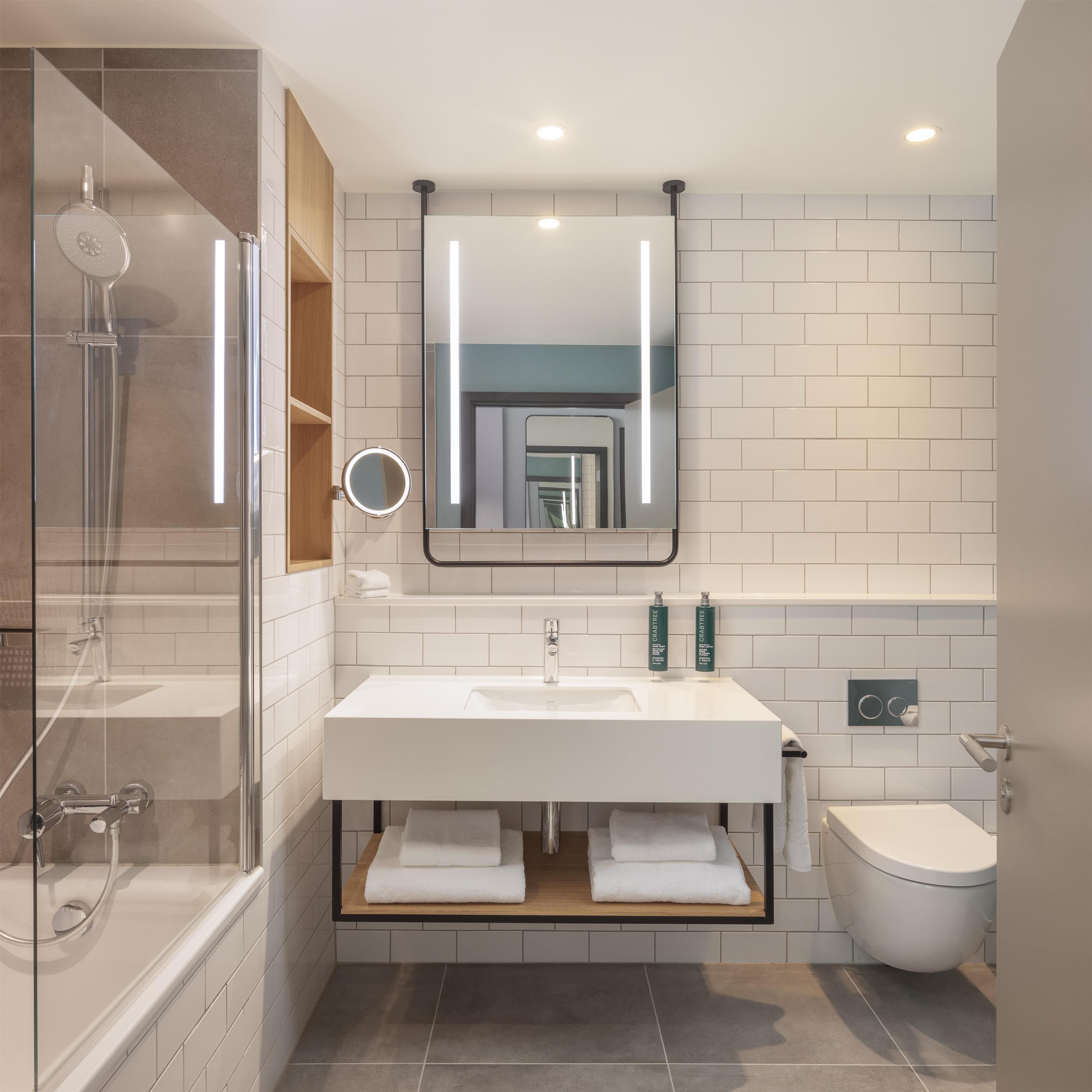 A modern bathroom with a glass shower enclosure, a white sink with a mirror above, and a toilet.