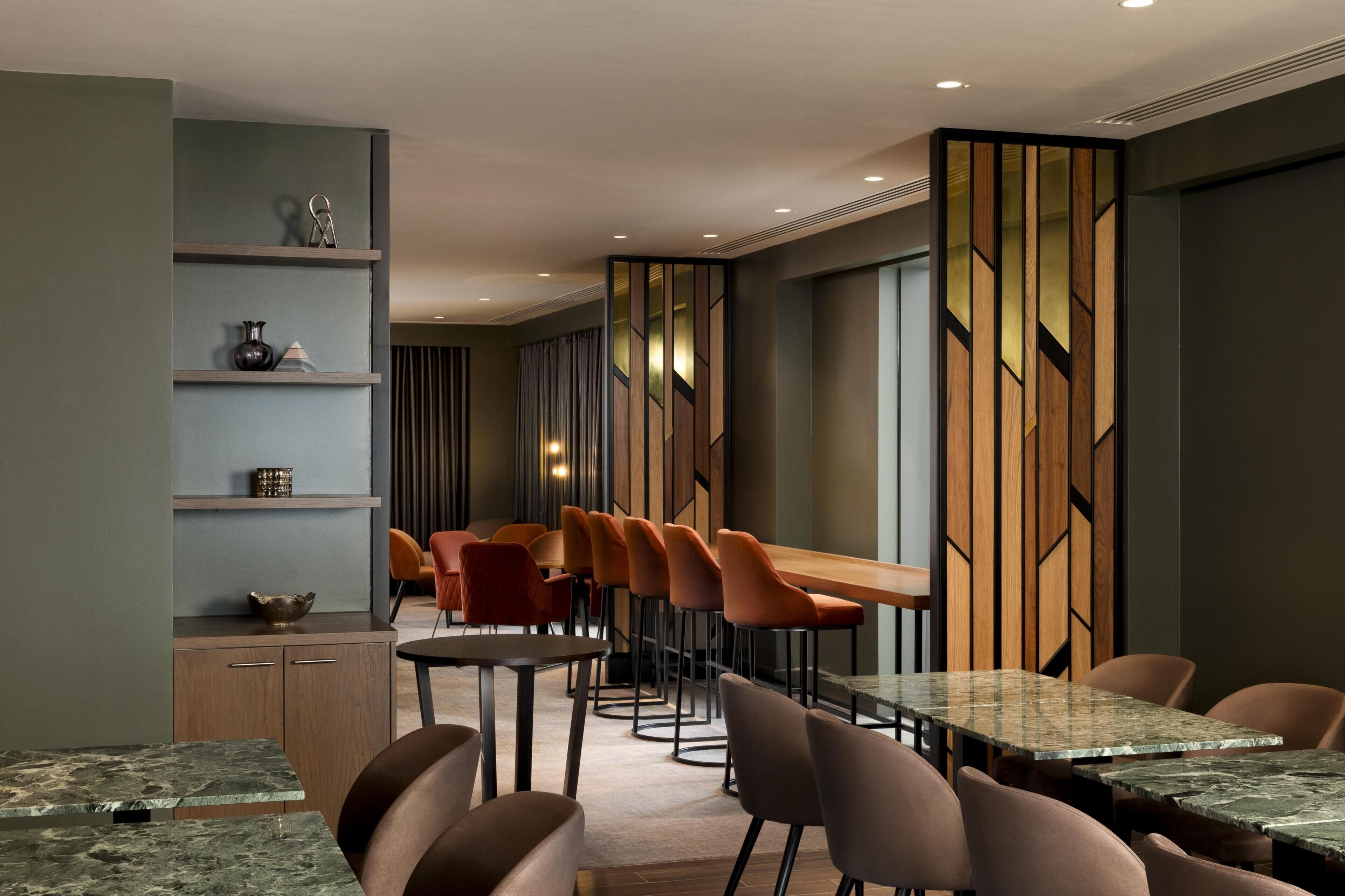 A modern dining area with multiple tables and chairs, a wooden partition with geometric patterns, and a wall-mounted shelf with decorative items.