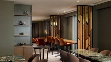 A modern dining area with multiple tables and chairs, a wooden partition with geometric patterns, and a wall-mounted shelf with decorative items.