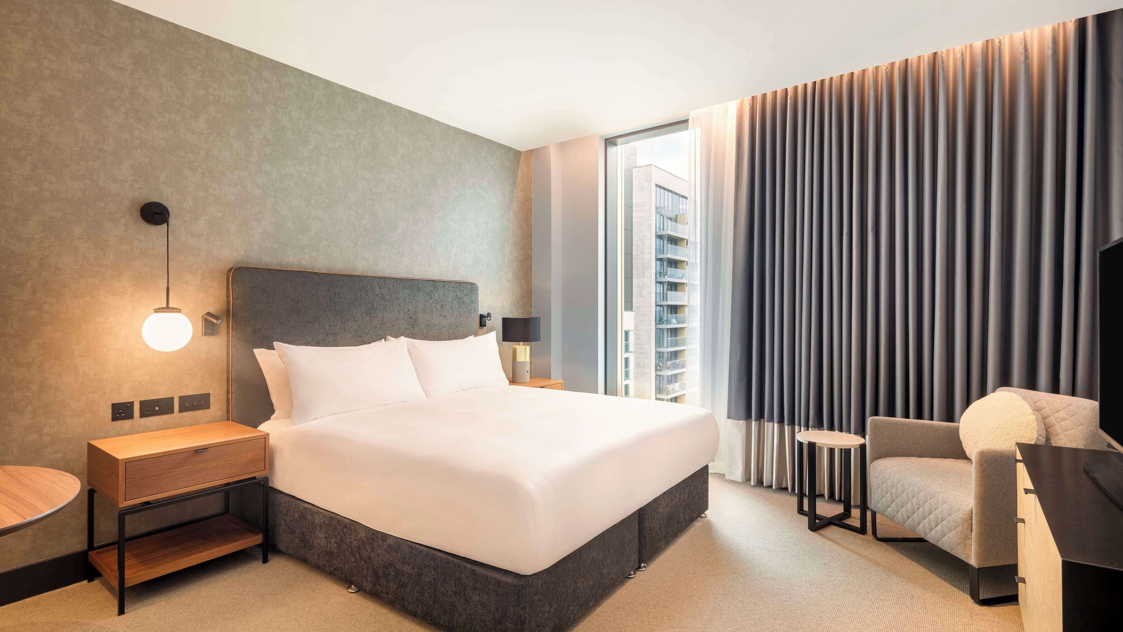 A modern hotel room with a large bed, bedside tables, a desk, and a chair.