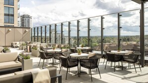 Una terraza en la azotea con mobiliario exterior, ventanas amplias y vistas de la ciudad.