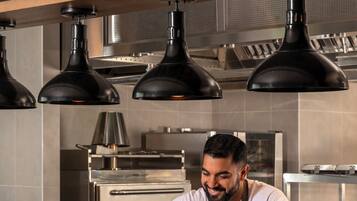 A chef in a modern kitchen with industrial lighting and stainless steel appliances.