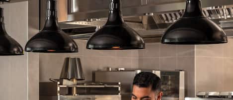 A chef in a modern kitchen with industrial lighting and stainless steel appliances.