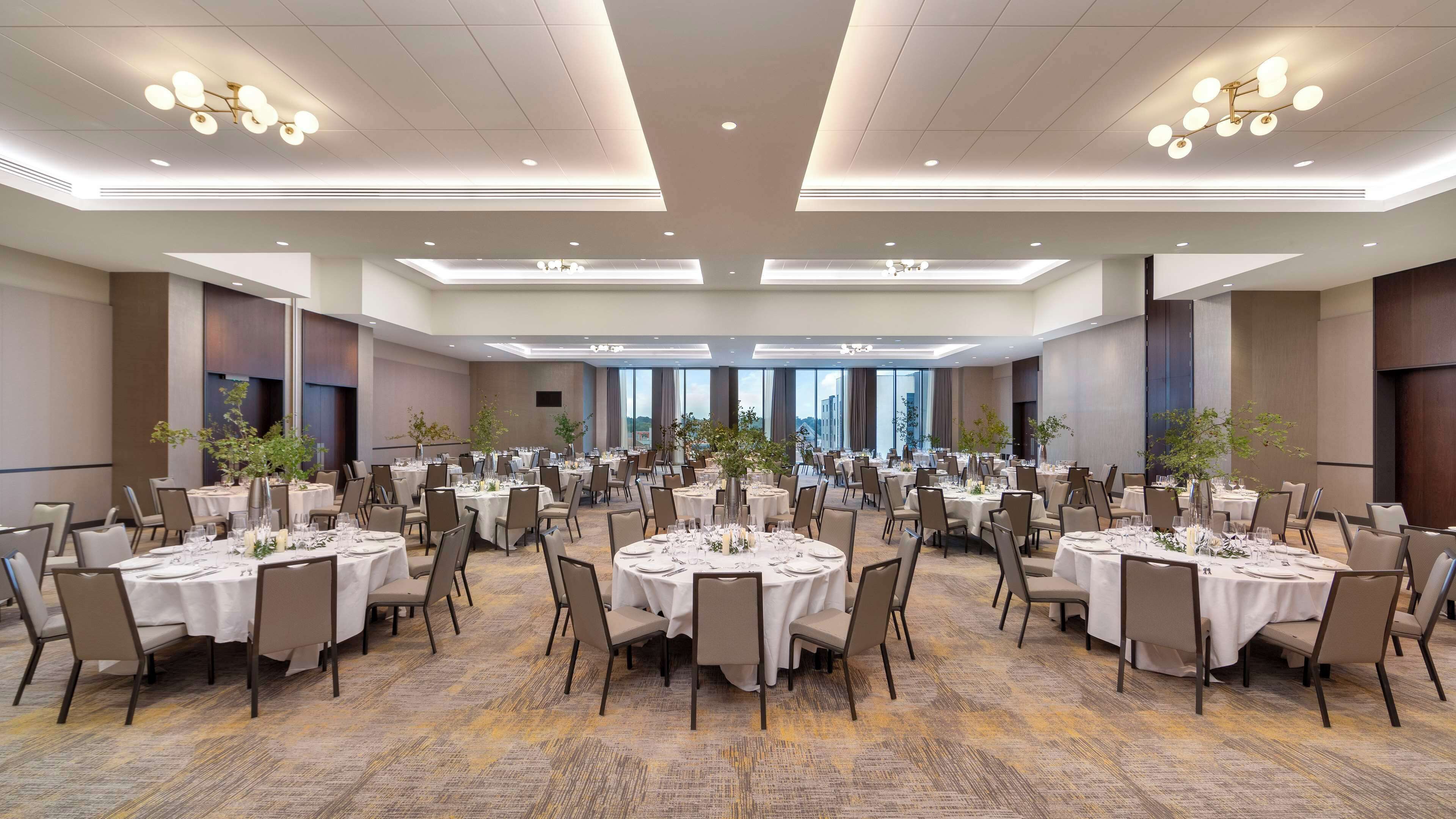 Un gran salón de banquetes con mesas redondas dispuestas para cenar, con piso alfombrado y techo alto con iluminación empotrada.