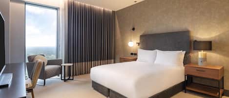 A modern hotel room with a large bed, a desk, a chair, and a view of the city.
