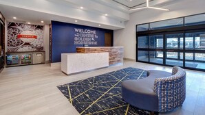 A modern reception area with a "Welcome The Centre of the Golden Horseshoe" sign, a reception desk, a patterned rug, and a seating area. - Hampton Inn & Suites by Hilton Burlington Toronto (Burlington)