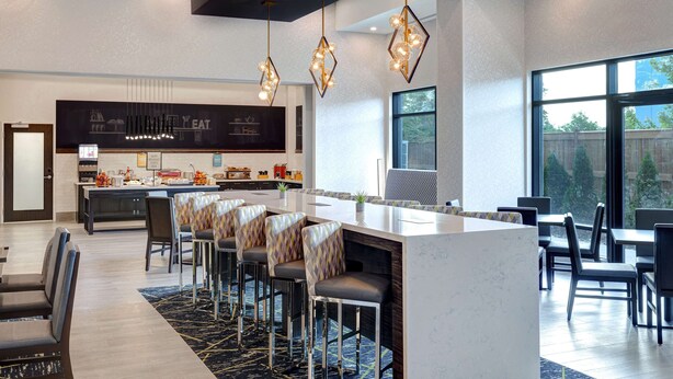 A modern hotel lobby with a central bar area, seating arrangements, and a view through large windows. - Hampton Inn & Suites by Hilton Burlington Toronto (Burlington)