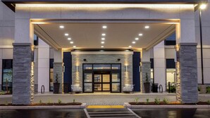 A modern hotel entrance with a covered walkway, stone pillars, and a glass door entrance. - Hampton Inn & Suites by Hilton Burlington Toronto (Burlington)