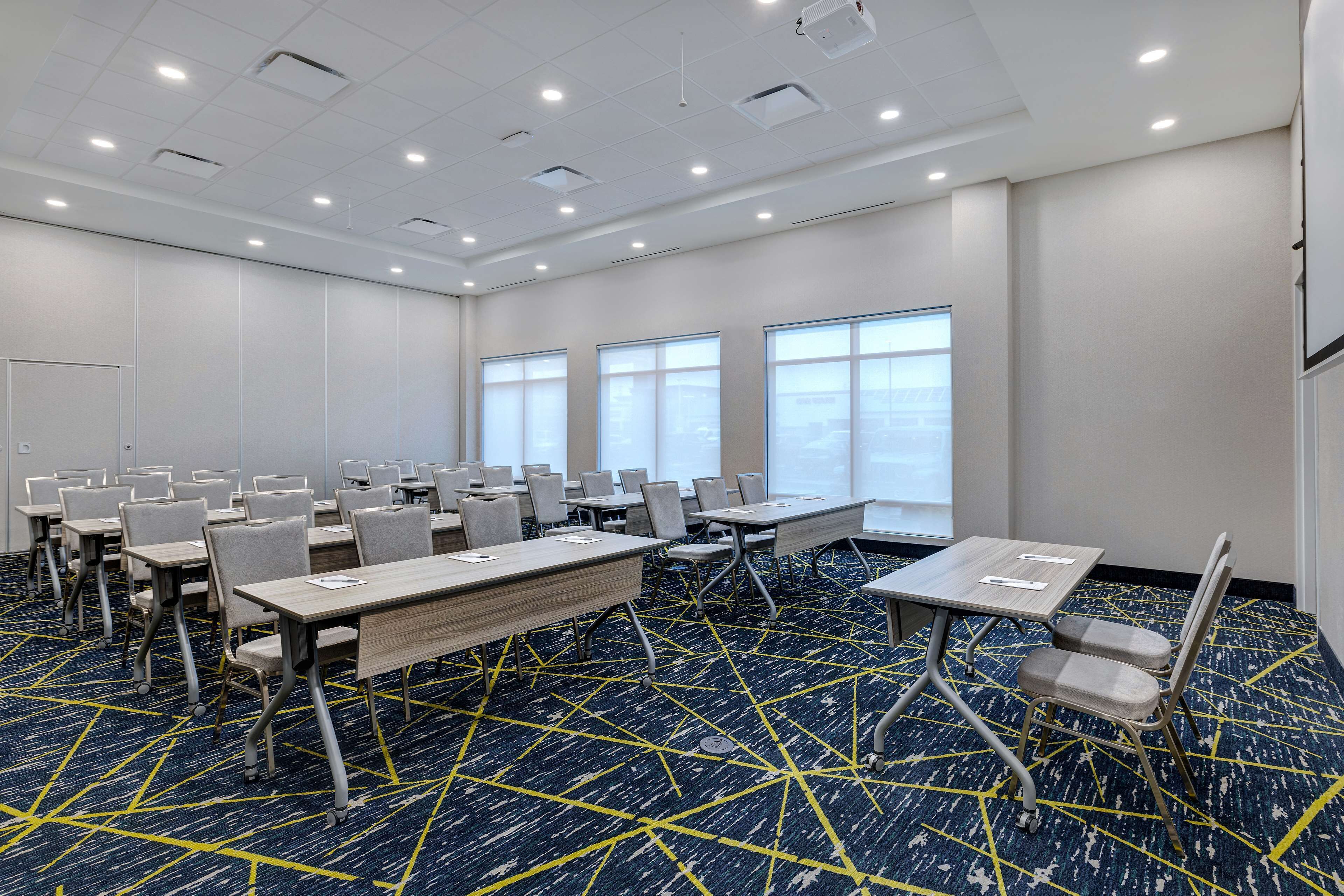 A conference room with multiple tables and chairs, large windows, and a patterned carpet.