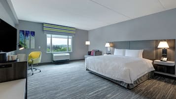 Una camera d'albergo con un letto grande, una scrivania, una sedia, una finestra con vista e una lampada.