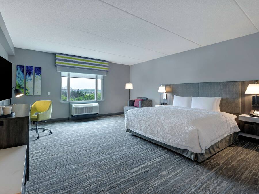 A hotel room with a large bed, a desk, a chair, a window with a view, and a lamp.