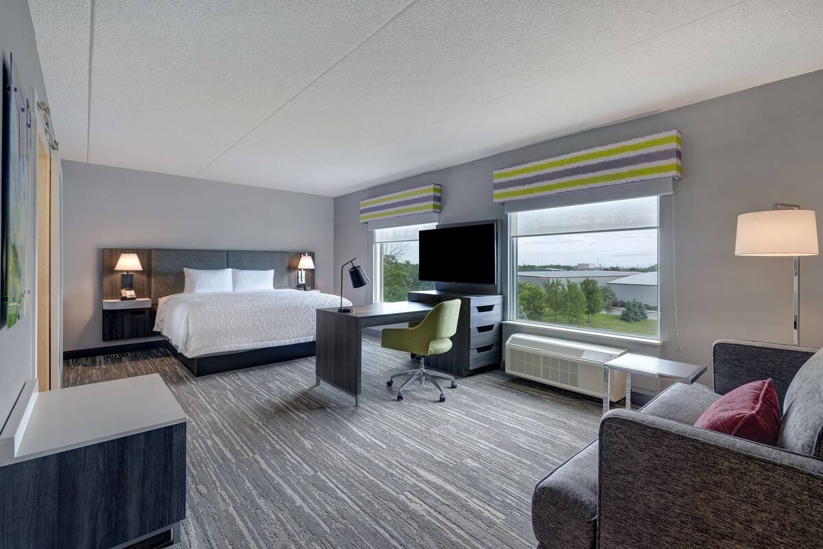 A hotel room with a bed, desk, TV, and a view of the outdoors.