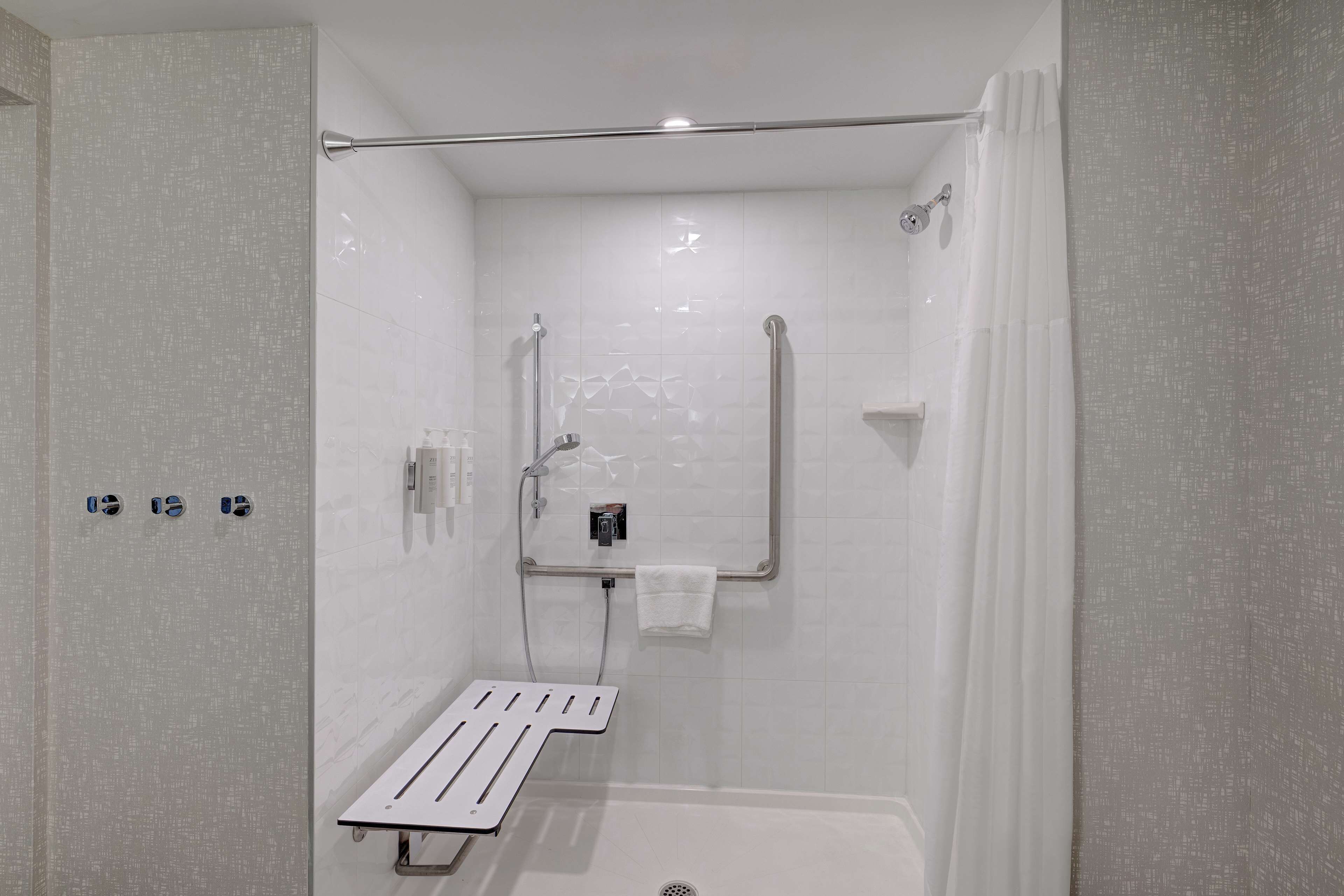 A modern bathroom with a shower, grab bars, and a towel rack.