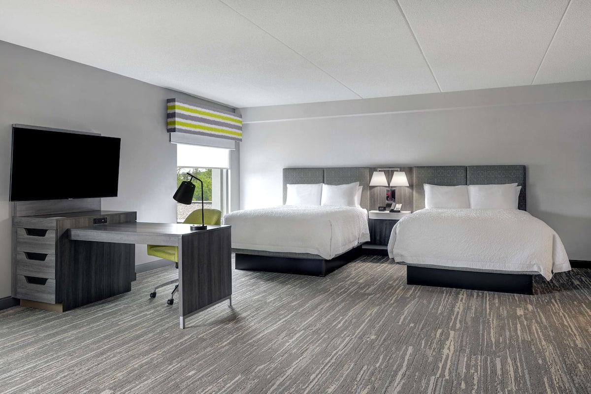 A hotel room with two beds, a desk, a TV, and a window with a view.