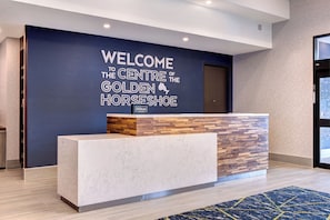 A reception desk with a wooden and marble design, a blue wall with a welcome sign, and a patterned carpet.