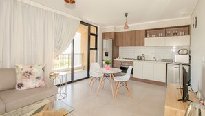 Eine moderne Wohnung mit Wohnzimmer, Essbereich und Küche. Es gibt ein Sofa, einen Esstisch mit Stühlen, eine Küchenarbeitsplatte und einen Fernseher.