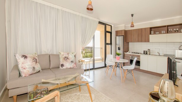 Ein modernes Wohnzimmer mit einer Couch, einem Glastisch und einem Essbereich mit kleinem Tisch und Stühlen.