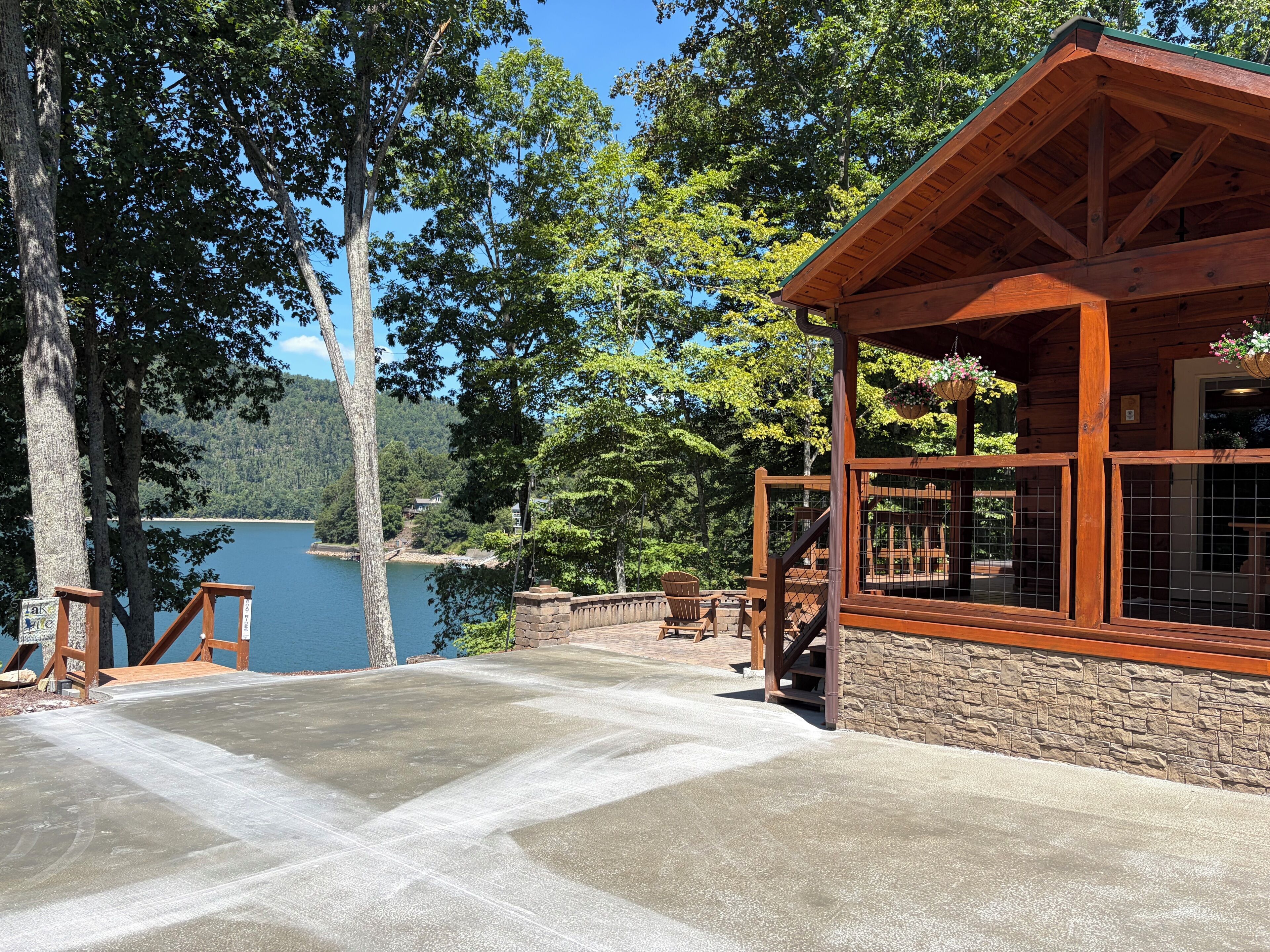 A wooden cabin with a stone foundation, a concrete patio, and a view of a lake.