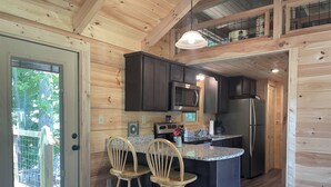Une cuisine moderne avec des murs en bois, un îlot central doté de tabourets de bar, des appareils en acier inoxydable et une vue dégagée sur l’extérieur grâce à une porte vitrée.
