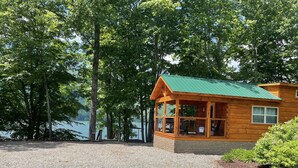 Une cabane en bois avec un toit vert, entourée d’arbres et bordée d’un chemin de gravier.